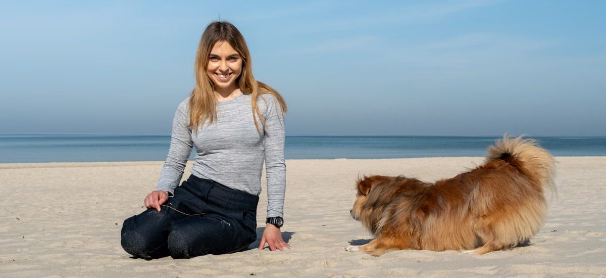 A woman playing with her dog on the sandy beach of Kołobrzeg on a sunny day.