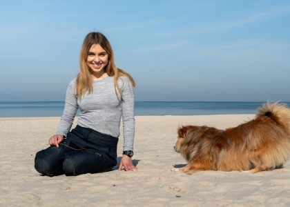 A woman playing with her dog on the sandy beach of Kołobrzeg on a sunny day.